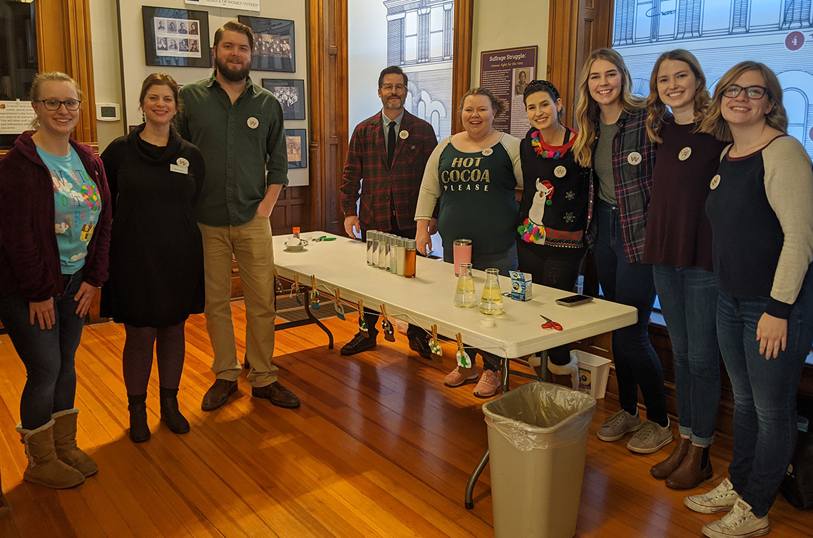 Nine white men and women standing around a table filled with activity supplies and smiling